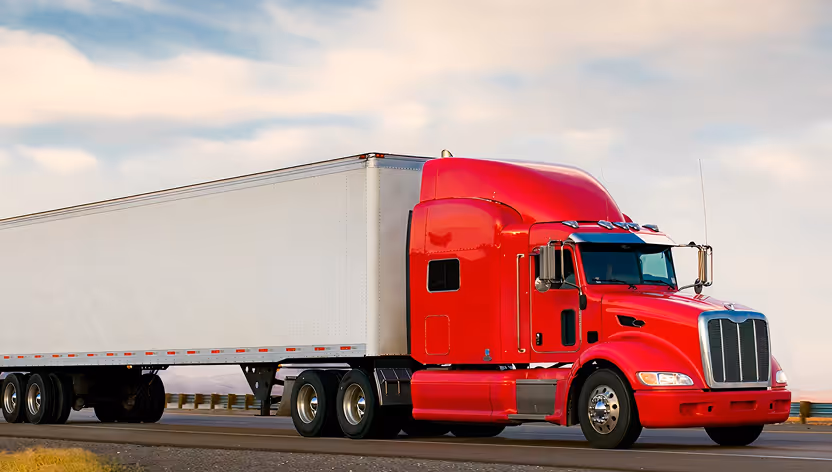 Bright red semi-truck with a white trailer driving on a highway under a cloudy sky.